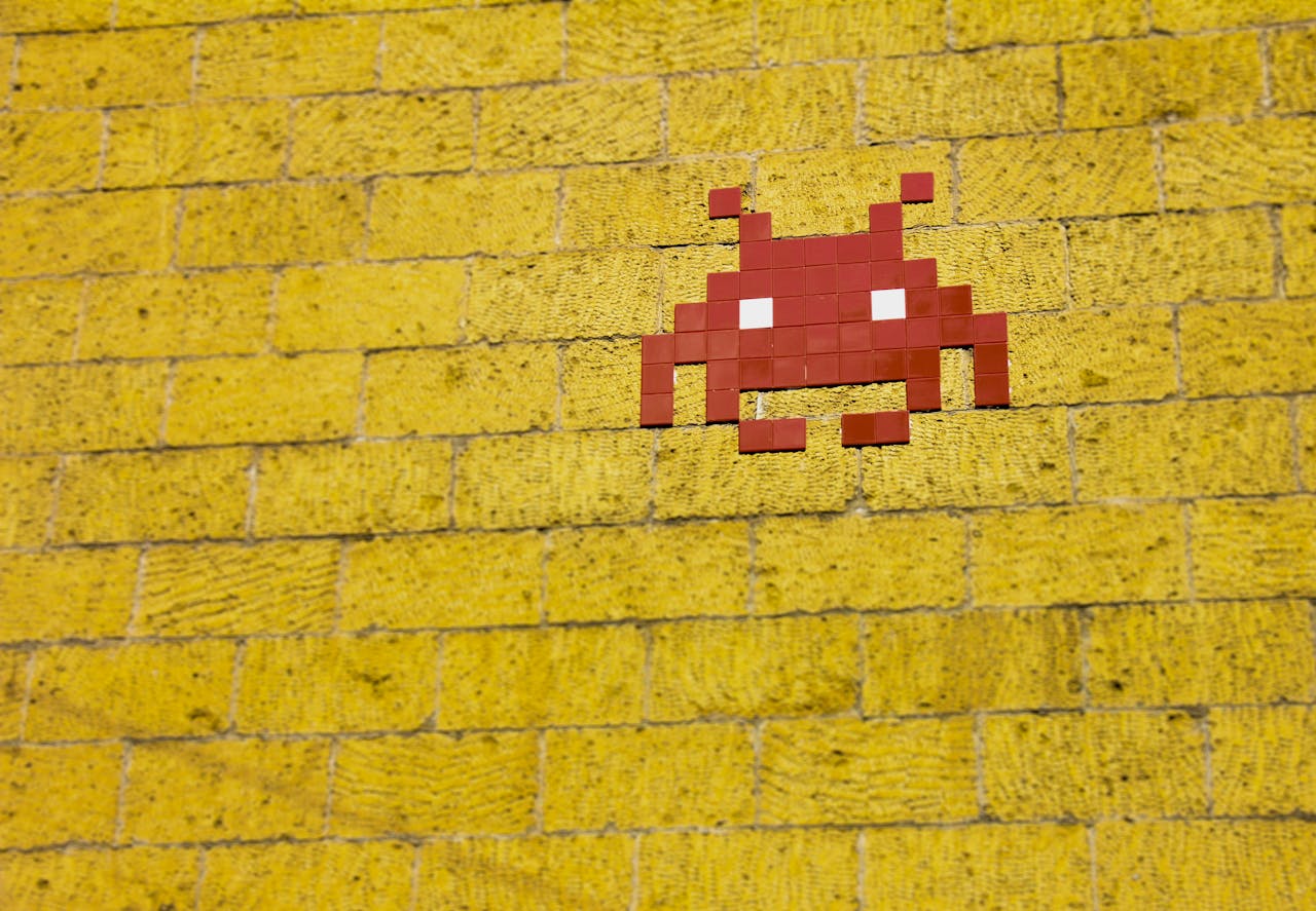 Street art featuring a retro pixelated space invader on a vivid yellow brick wall.